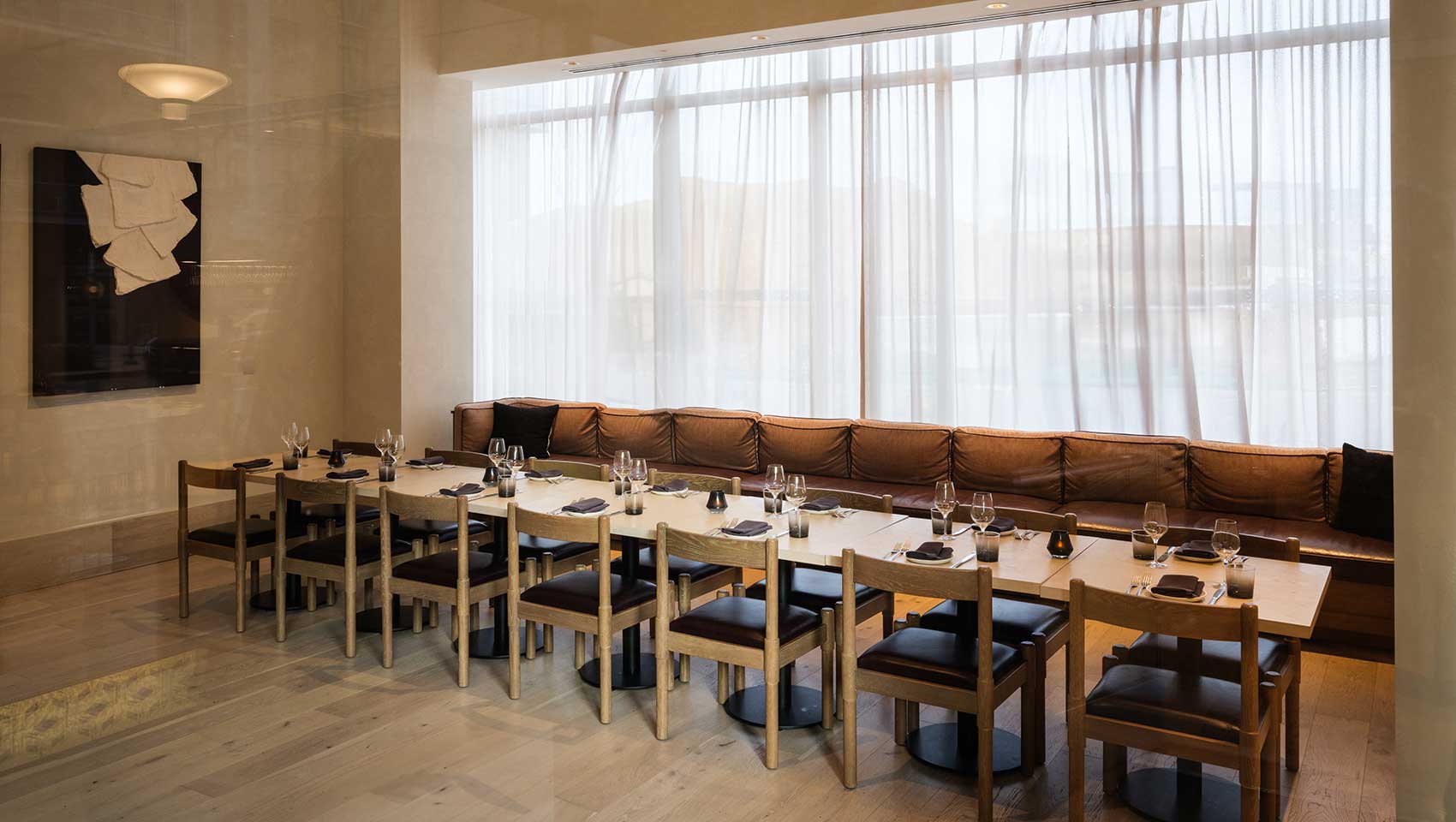 Private dining room with long cushioned bench seat along wall of windows with accent pillows, long table and chairs on either side