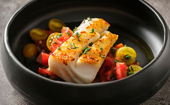 Fish dinner dish with tomatoes and seasoning in a black bowl